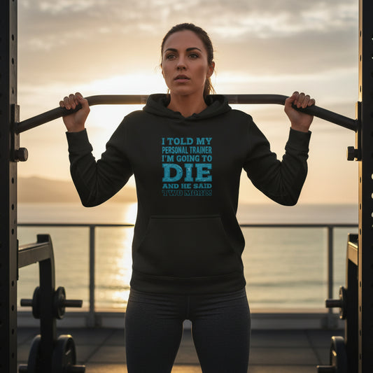 A woman wearing a black hoodie with humorous text at an outdoor gym with the sunset in the background.