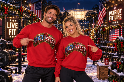 A man and a woman pose together in a festive outdoor gym setting at night, wearing matching red crewneck sweatshirts with a large, colorful, glittery 'PATRIOT' graphic across the chest. The background features holiday decorations, American flags, weights, and a sign reading 'PATRIOT FIT LIFE'.