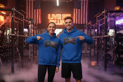 A man and a woman standing in a gym wearing matching blue hoodies with a colorful Halloween PATRIOT graphic design across the chest. The background features a neon sign reading 'LIVE FIT FIT LIFE,' American flags, weight racks, and fog.