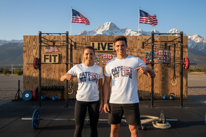 A man and a woman standing in front of a wooden outdoor gym backdrop with mountains and American flags behind them, both wearing white graphic T-shirts that read 'PATRIOT FIT LIFE.'