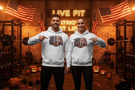 Two people standing in a gym wearing matching white hoodies with a Halloween patriotic graphic print on the front that reads "Patriot Fit Life" pointing at the chest design. The background features a brick wall, neon sign, American flags, weight racks, and jack-o'-lanterns.