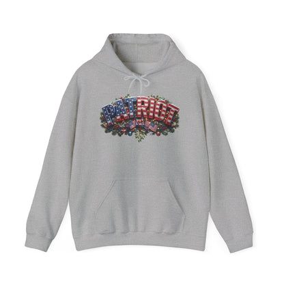 A light gray heather pullover hoodie with a Christmas PATRIOT festive chest graphic design featuring red and white striped gift boxes wrapped in the American flag, decorated with green pine branches and small red ornaments, shown on a plain white background.