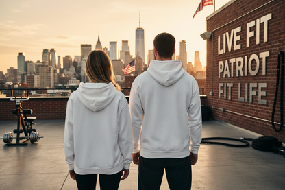 A man and a woman standing on a rooftop terrace at sunset, viewed from behind, wearing matching white hoodies. The background features a New York City skyline with the One World Trade Center, a brick wall with the text 'LIVE FIT and PATRIOT FIT LIFE,' and fitness equipment.