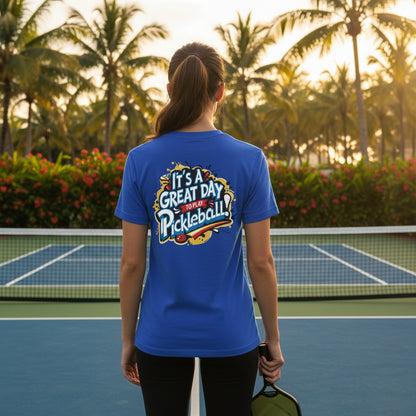 A woman on a pickleball court wearing a blue-colored t-shirt featuring an 'It's a Great Day To Play Pickleball!' text design.