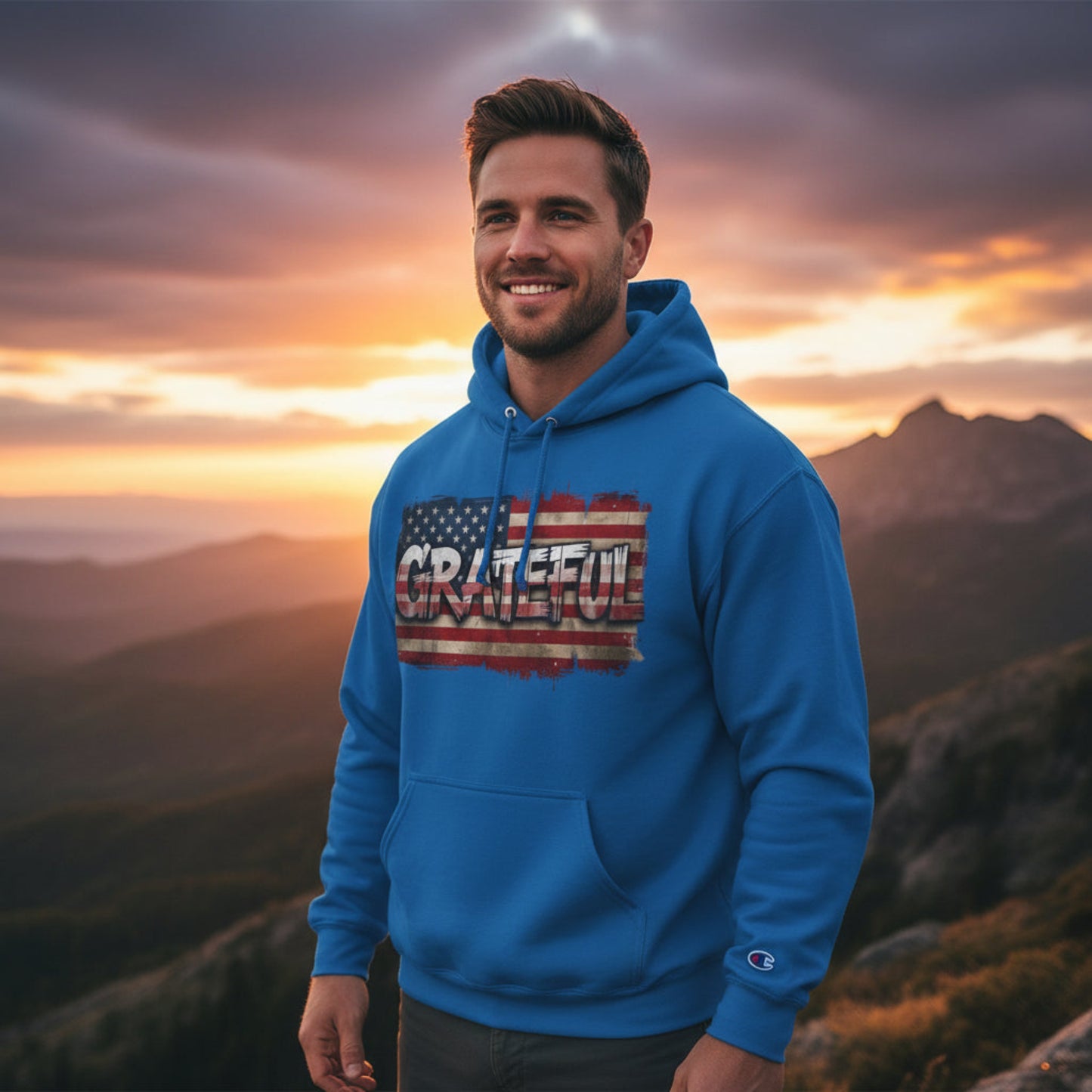 Man wearing a blue hoodie with 'Grateful' design against a mountain sunset