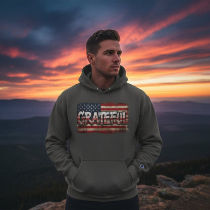 Man wearing a hoodie with 'Grateful' text and American flag design against a sunset mountain backdrop