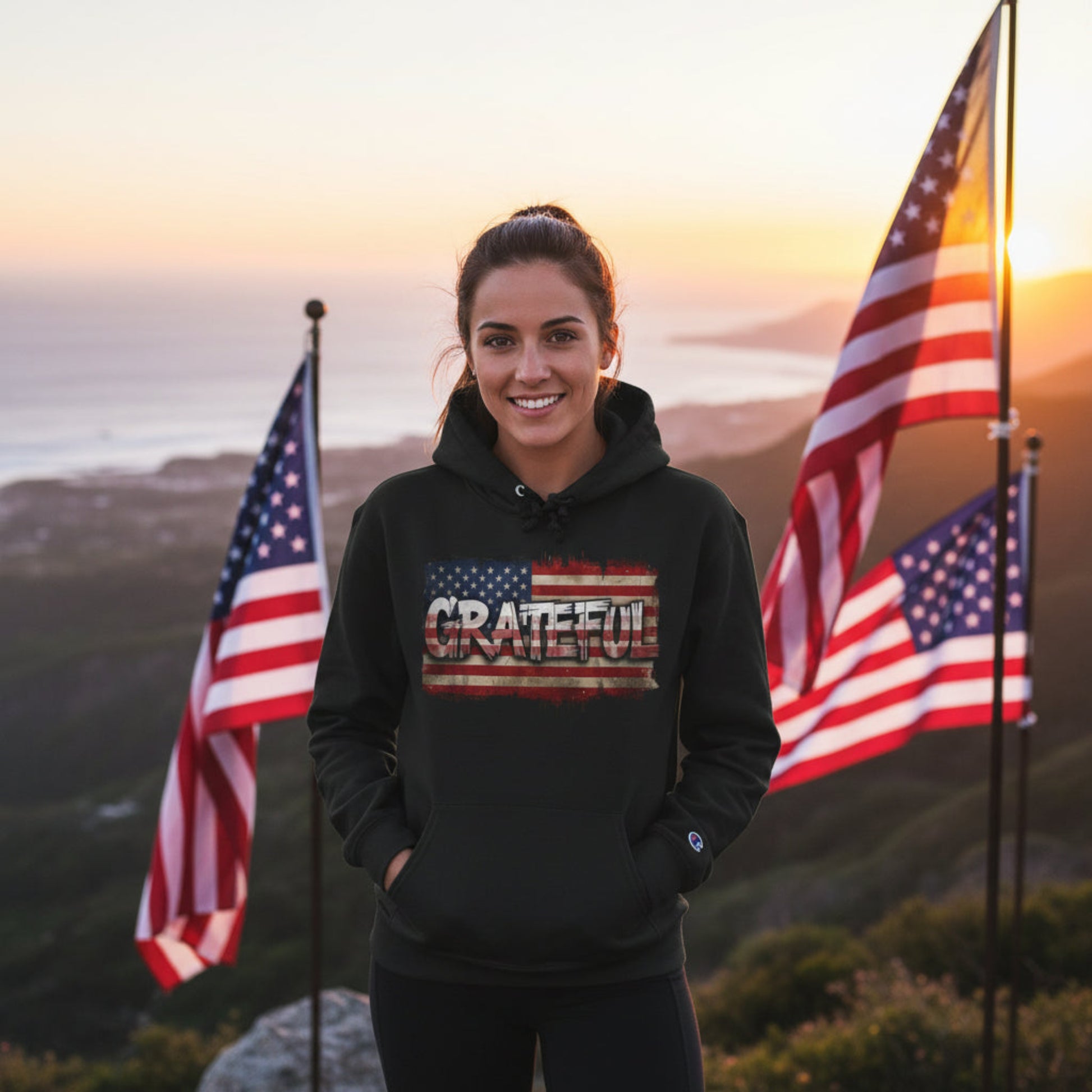 Woman wearing a black hoodie with 'GRATEFUL' text in front of American flags at sunset.