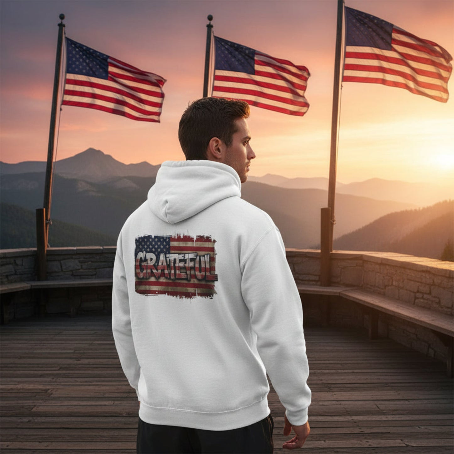 Man in a white hoodie with an American flag design standing on a wooden deck with American flags and a sunset in the background.