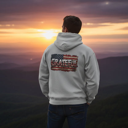 Person wearing a hoodie with 'Grateful' and an American flag design, standing against a sunset landscape.