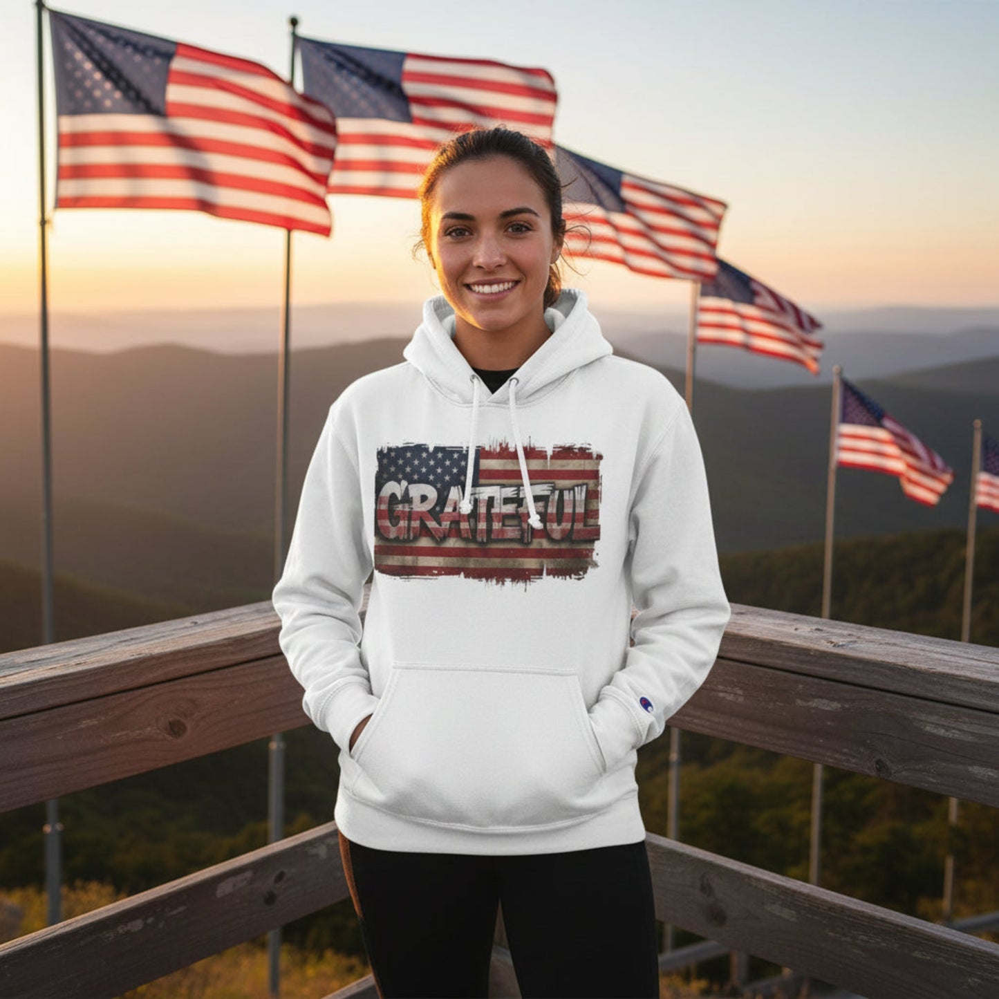 Woman wearing a white hoodie with 'GRATEFUL' design in front of American flags at sunset.