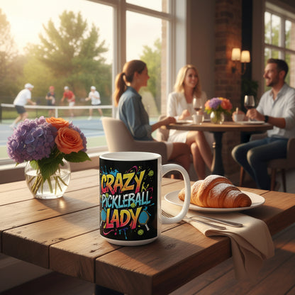 A ceramic mug with a colorful design that includes text and pickleball elements, displayed on a table with a pickleball game in the background.