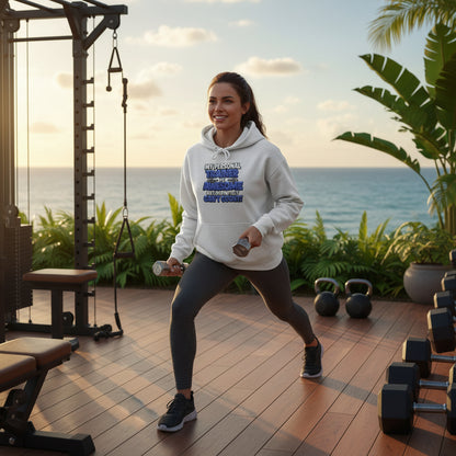 A woman wearing a gray hoodie with text on it that says, My Personal Trainer Is Awesome But Definitely Can't Count!, standing in an outdoor gym with a city skyline in the background.