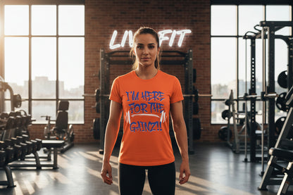 Woman wearing an orange t-shirt with motivational text I'm Here For The Gainz!! in a gym setting.