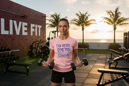 A woman holding dumbbells in a gym wearing a pink t-shirt that says I'm Here For The Gainz!! with palm trees and a sunset in the background.