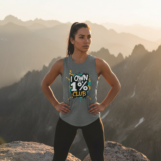 Woman wearing a gray tank top with the 'I Own the 1% Club' graphic design standing on a mountaintop.
