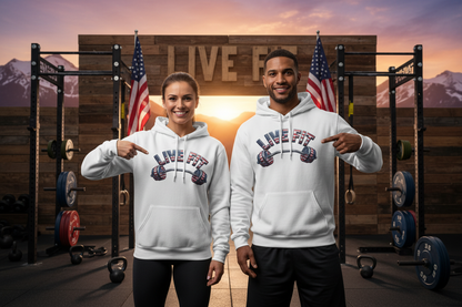 A man and a woman standing in a gym setting wearing matching white 'LIVE FIT' graphic hoodies, pointing at the chest print. The background features a wooden wall with 'LIVE FIT' text, American flags, weight racks, and mountains at sunset.