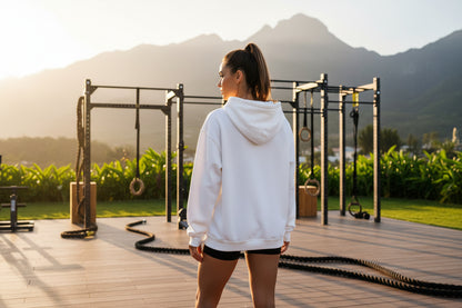 A woman in a white hoodie standing on a wooden deck with mountains in the background.