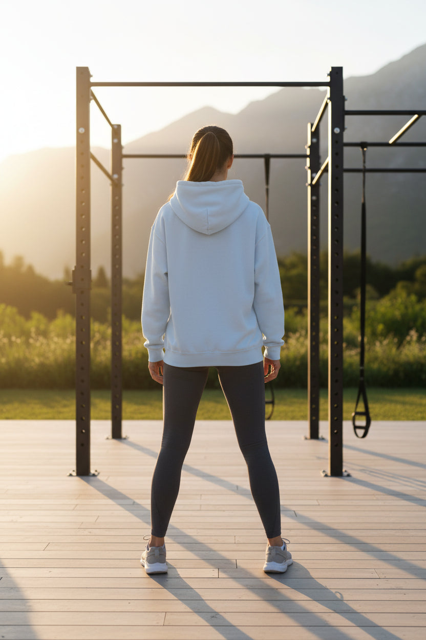 A woman in a light blue hoodie and black leggings standing on a wooden platform with mountains in the background.