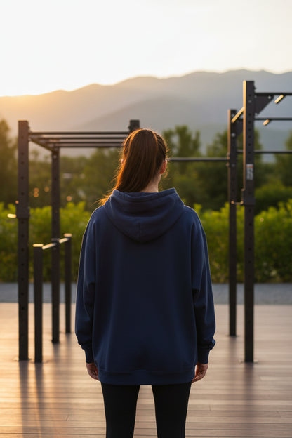 A woman wearing a navy blue hoodie standing on a wooden deck with mountains in the background.