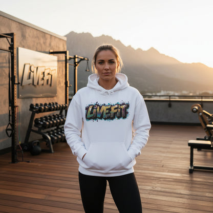 A woman wearing a white hoodie with 'LIVE FIT' text in a colorful design on a wooden floor in an outside gym setting with mountains in the background.