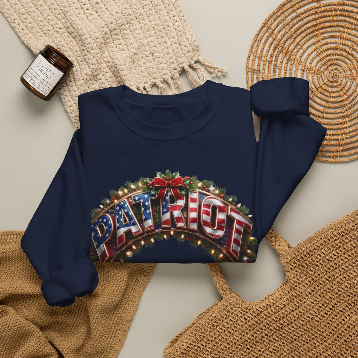 A navy blue long-sleeve crewneck sweatshirt with a festive graphic reading 'PATRIOT' in red, white, and blue flag lettering under a green holiday wreath.