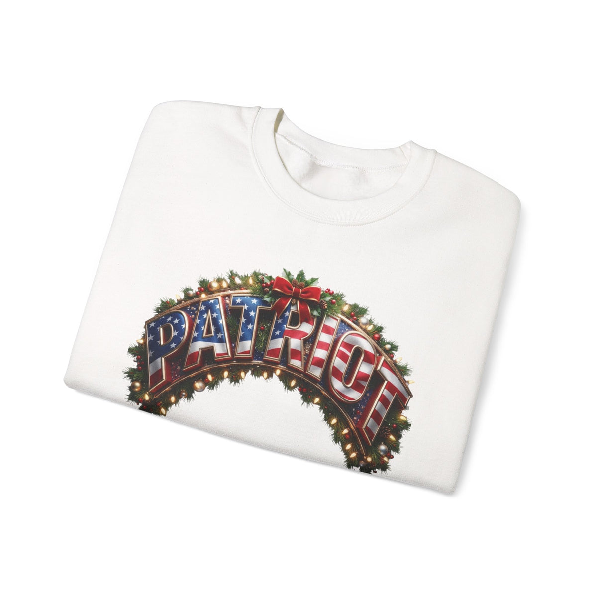 A folded white crewneck sweatshirt featuring a festive graphic on the front. The graphic displays the word 'PATRIOT' in a 3D-effect lettering filled with the American flag pattern, framed by a green holiday wreath with red bows and warm glowing lights, set against a plain white background.