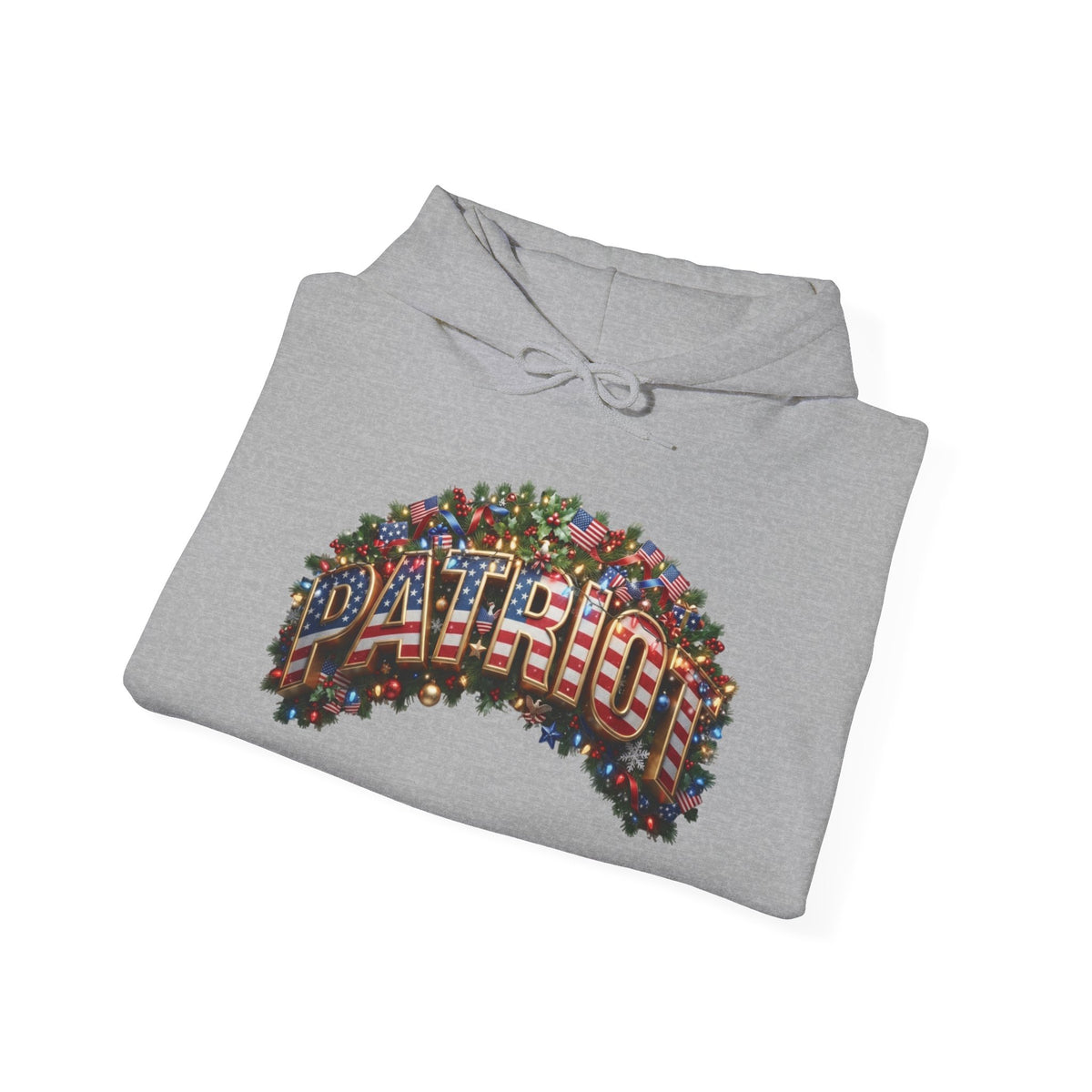 A folded light gray hoodie on a white background, featuring a large graphic on the front with the word 'PATRIOT' in red, white, and blue American flag patterned letters, surrounded by green pine branches and small holiday lights.