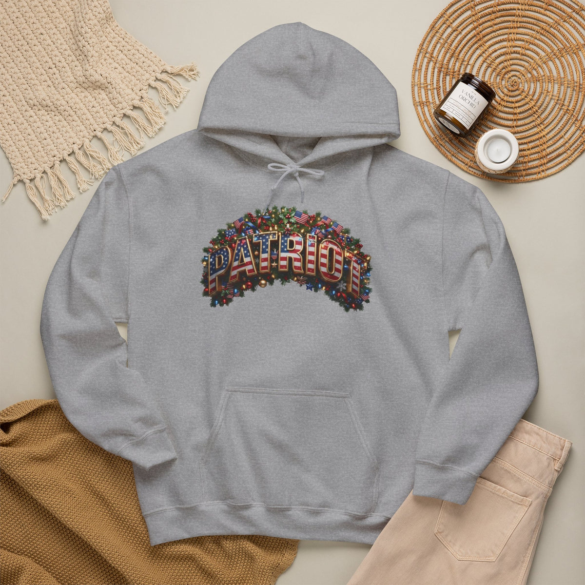 A light gray pullover hoodie laid flat on a beige surface, featuring a colorful festive 'PATRIOT' graphic across the chest.