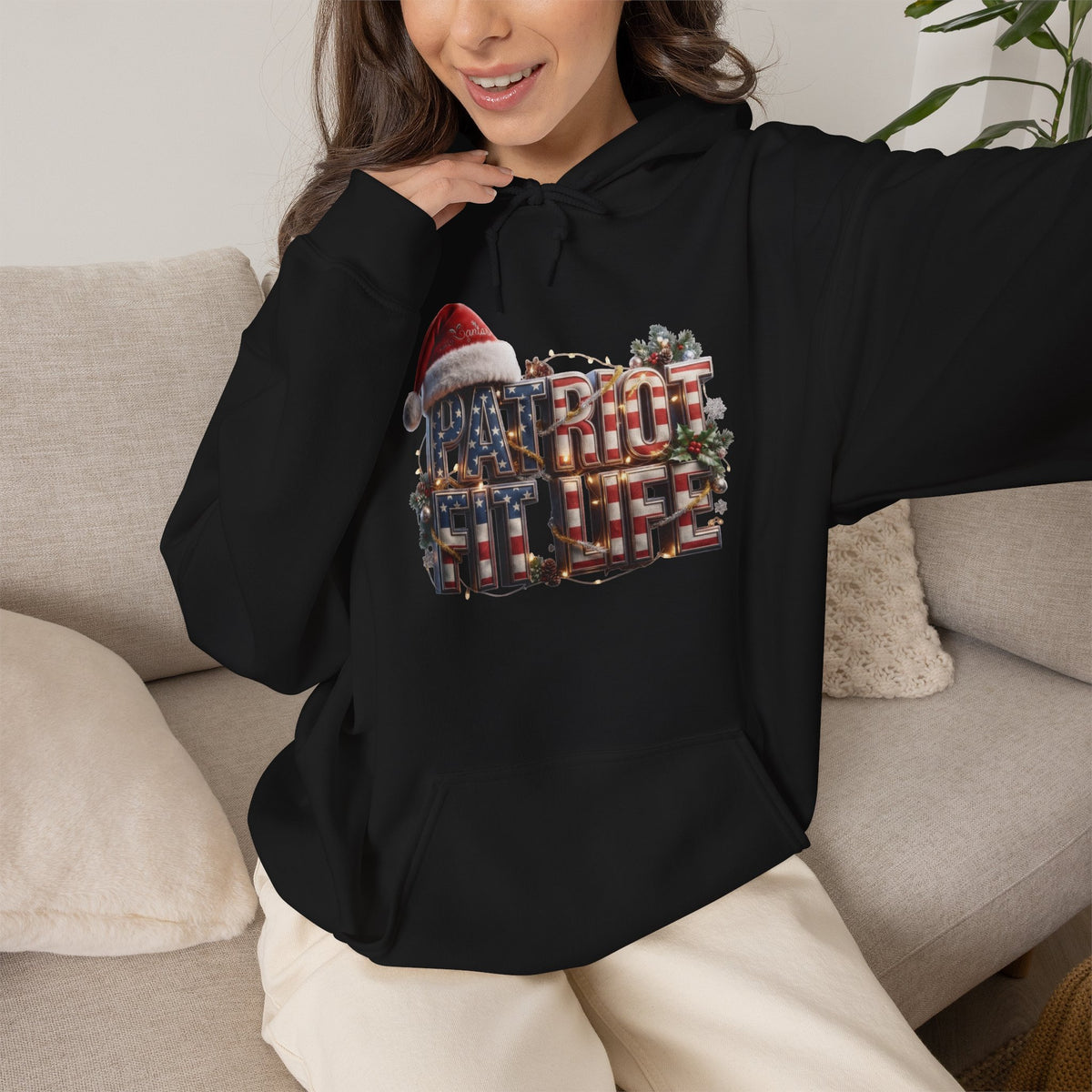 A woman wearing a black hoodie with a festive PATRIOT FIT LIFE American flag design, sitting on a couch.