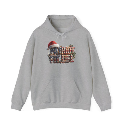 A light gray heather pullover hoodie with a festive Christmas-themed graphic on the chest. The graphic features the text 'PATRIOT FIT LIFE' in an American flag pattern styled with red, white, and blue, a red Santa hat, and green pine branches.