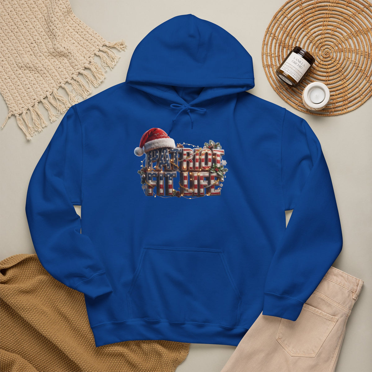 A royal blue pullover hoodie laid flat on a light beige surface, featuring a festive chest graphic that reads 'PATRIOT FIT LIFE' in red, white, and blue with a Santa hat.