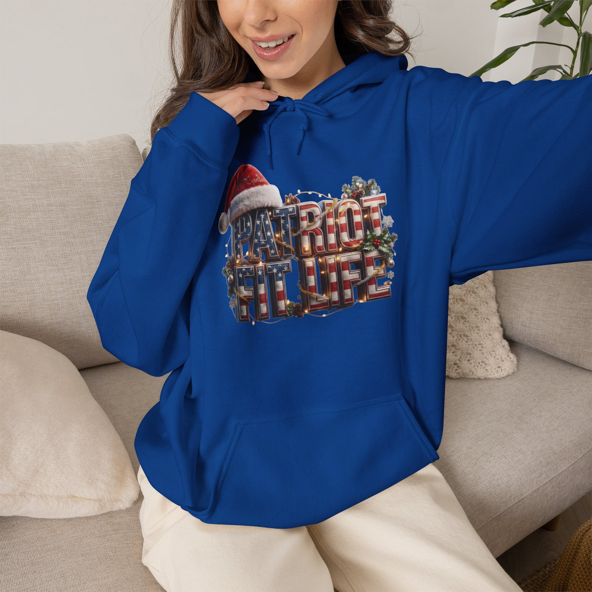 A woman wearing a royal blue hoodie with a festive 'PATRIOT FIT LIFE' graphic, sitting on a beige couch.
