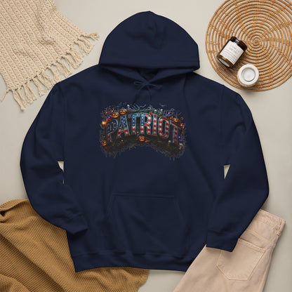 A navy blue hoodie laid flat on a light beige surface, decorated with a colorful 'PATRIOT' graphic featuring pumpkins and autumn leaves. The hoodie is styled with a tan knit blanket, beige pants, a woven placemat, and small jars.