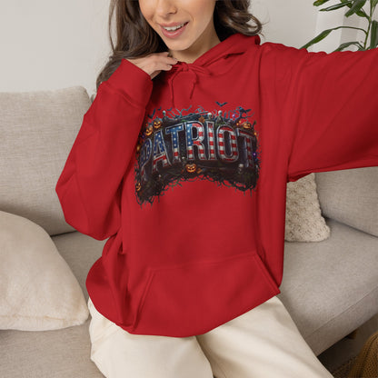 A woman wearing a bright red hoodie with a large 'PATRIOT' graphic across the chest featuring a patriotic American flag and Halloween elements like pumpkins and bats, sitting on a light gray couch.