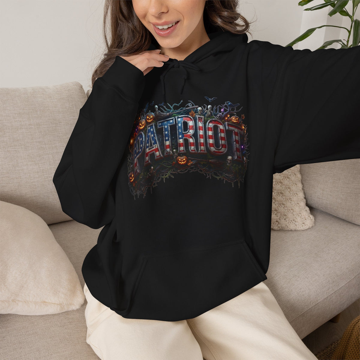 A woman wearing a black hoodie with the word "PATRIOT" and Halloween design, sitting on a couch.