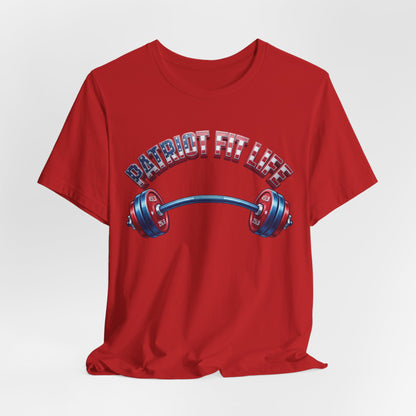 A red short-sleeve crewneck t-shirt featuring a graphic of a barbell with an American flag pattern and the text 'PATRIOT FIT LIFE' arched above it, displayed on a light gray background.