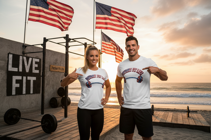 A man and a woman are standing on a beach at sunset, wearing matching white t-shirts with a red, white, and blue graphic that reads 'Patriot Fit Life' and pointing to the logos. Behind them are American flags, a pull-up bar, and a concrete wall with 'LIVE, FIT' written on it.