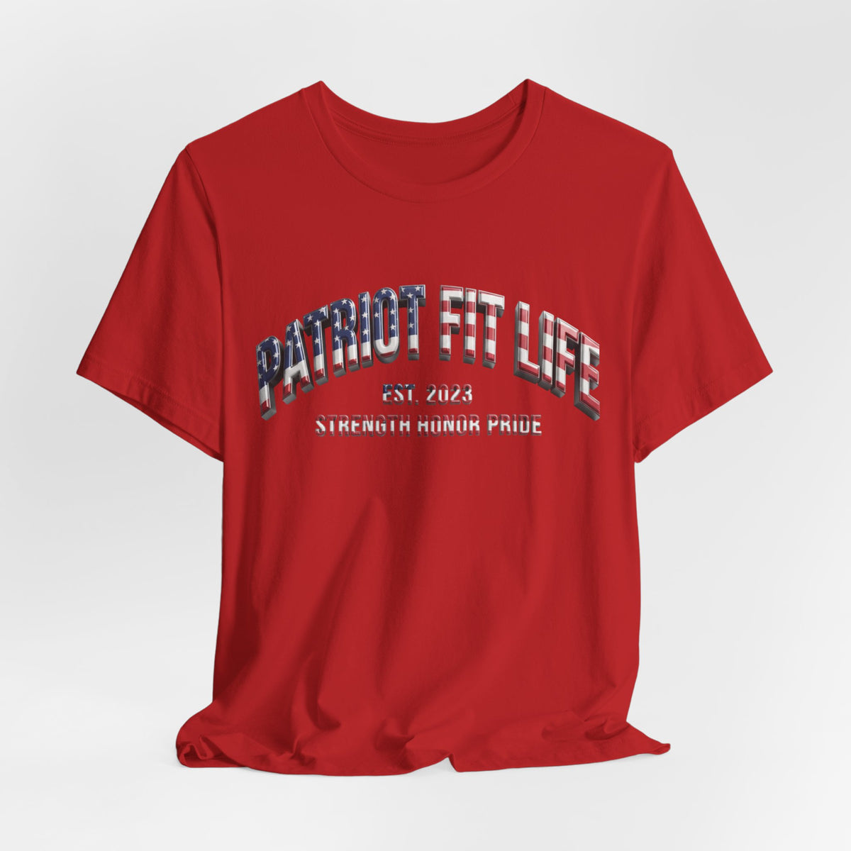 A red short-sleeve crewneck t-shirt with a graphic on the chest reading 'PATRIOT FIT LIFE EST. 2023 STRENGTH HONOR PRIDE' in a distressed, patriotic-themed font, shown against a light gray gradient background.