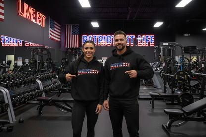 A man and a woman are standing in an indoor gym, both wearing black hoodies with a patriotic red, white, and blue graphic on the chest that reads 'PATRIOT'.