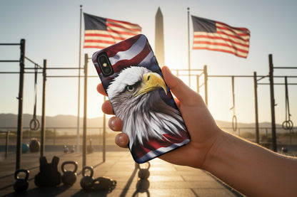 A phone case with a bald eagle and American flag design held in front of American flags and an outdoor gym.