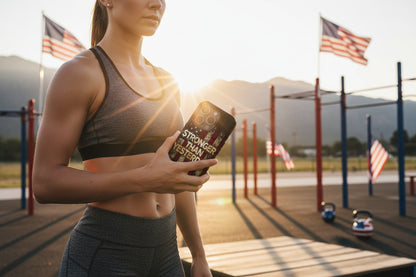 Person showing a Stronger Than Yesterday phone case with an outdoor setting and American flags in the background.