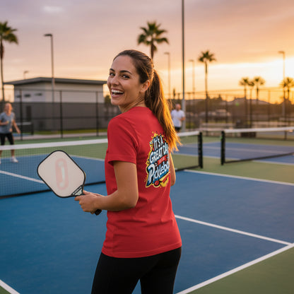 A woman on a pickleball court wearing a red-colored t-shirt featuring an 'It's a Great Day To Play Pickleball!' text design.