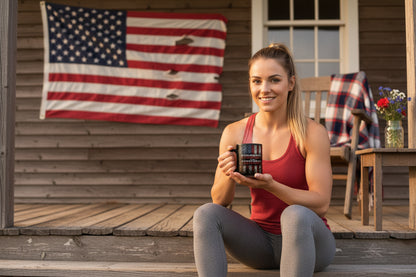 A woman holding a mug that says Stronger Than Yesterday sitting on a wooden porch with an American flag in the background.
