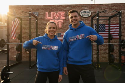 A man and a woman are standing in an outside gym wearing matching bright royal blue hoodies with the UNSTOPPABLE! print on the chest, and they are both pointing at the text. The background features a brick wall with a neon LIVE FIT sign, weight racks, and American flags.
