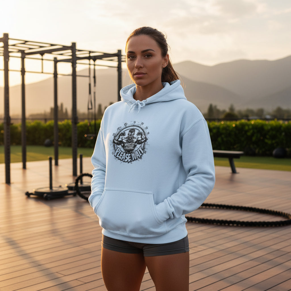 A woman wearing a light blue hoodie with a graphic design that says Muscles Loading Please Wait in an outdoor gym background.