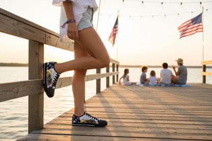 A woman standing on a wooden dock showing an American flag bald eagle sneaker design with American flags and people in the background.
